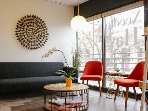 Waiting room at Needle in the Hay: a gray sofa, two orange chairs, and the salon name reversed on the street window.